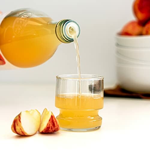 Pouring apple juice into a glass with apple slices nearby.